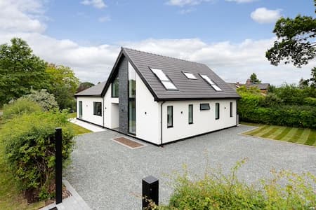 Modern white rendered house with roof windows in a dark tiled roof, set in landscaped gardens