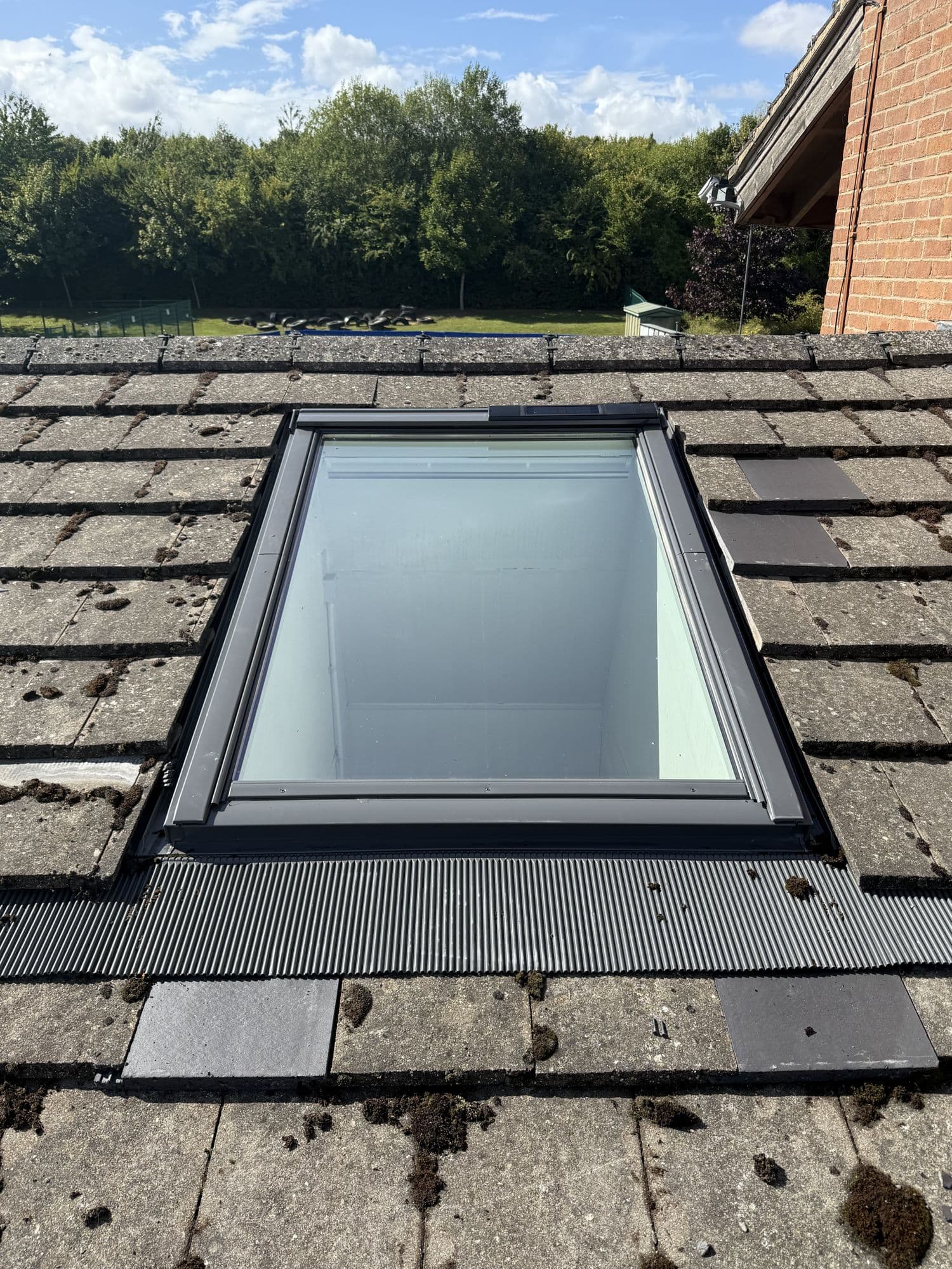 Concrete roof tiles around a roof window with new grey flashing