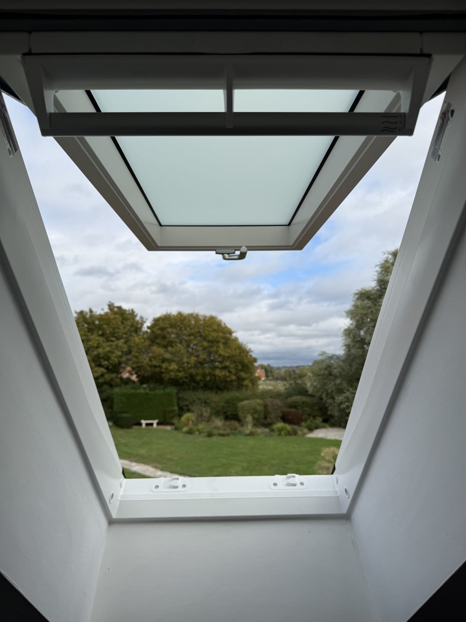 View up through an open roof window to trees and a garden