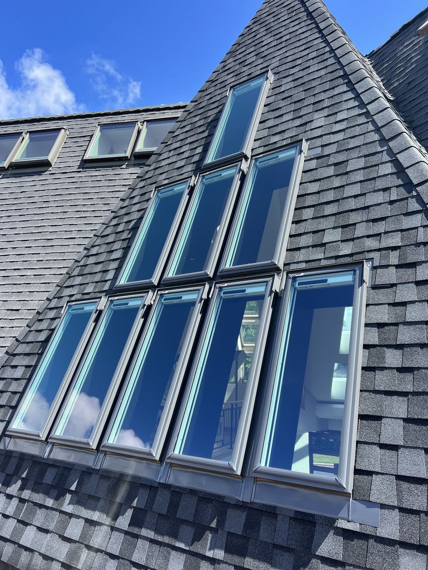 A bank of tall roof windows set into a steep grey roof under a blue sky